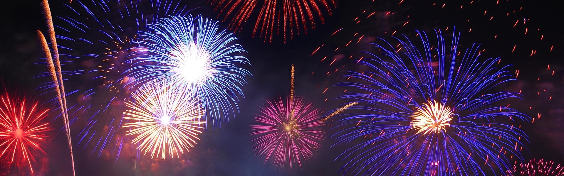 Panoramic image of night sky filled with colorful firework plumes and explosions.