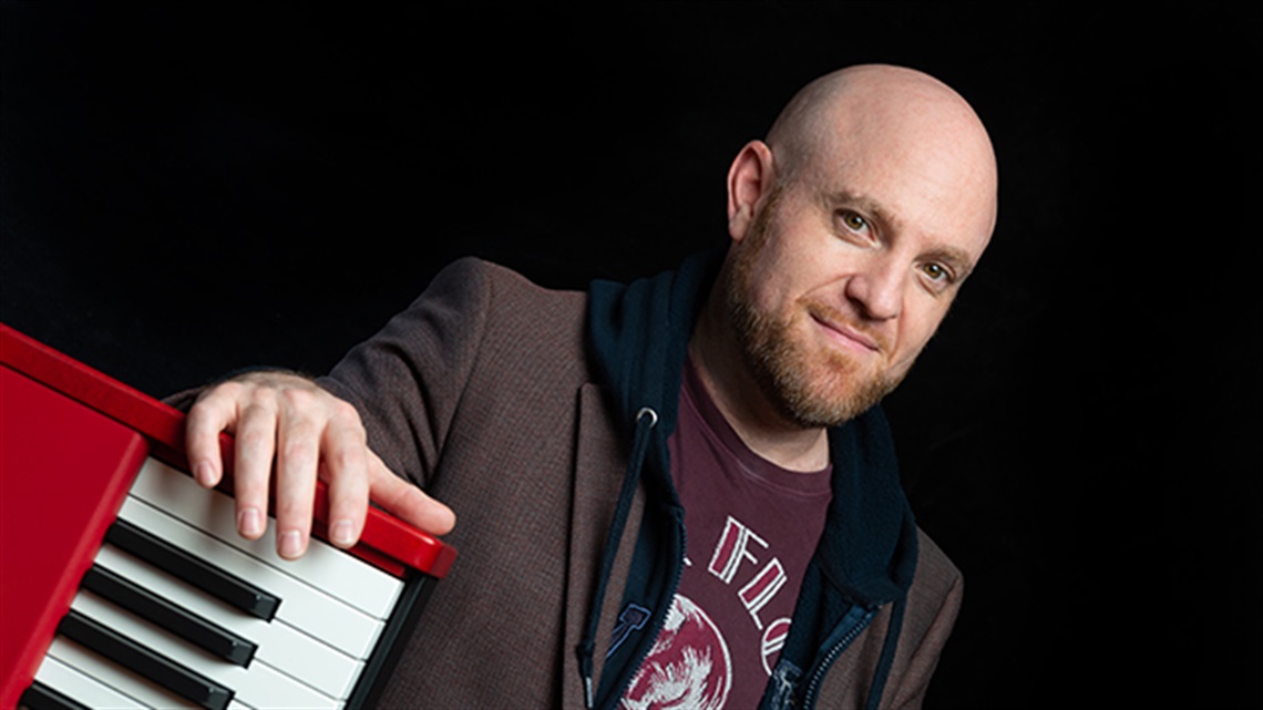 Photo of Jazz musician Lao Tizer on black background, leaning on a red keyboard