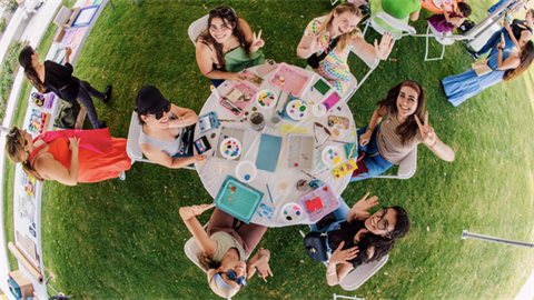 Art workshop attendees at a round table looking up at photographer