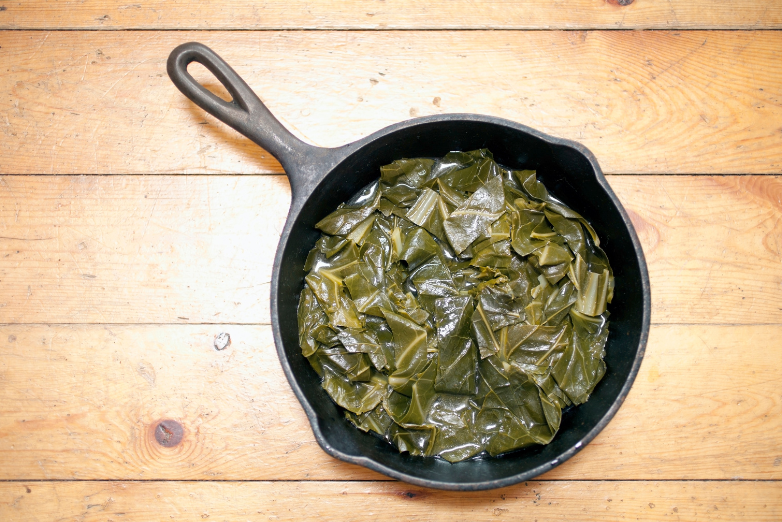 Overhead shot of collard greens in a black cast iron skillet. Skillet is on a rustic wood surface.