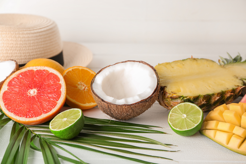 Fresh tropical fruits, including oranges and mangoes, displayed with citrus, coconut, and pineapple to accompany a DIY Orange + Mango Electrolyte Refresher recipe.