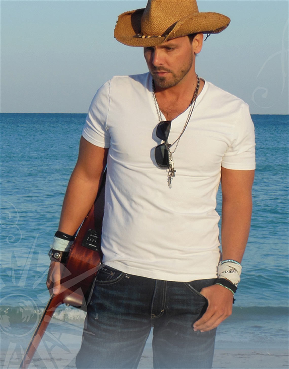 Photo of Tim Charron wearing a cowboy hat, carrying his guitar at the beach.