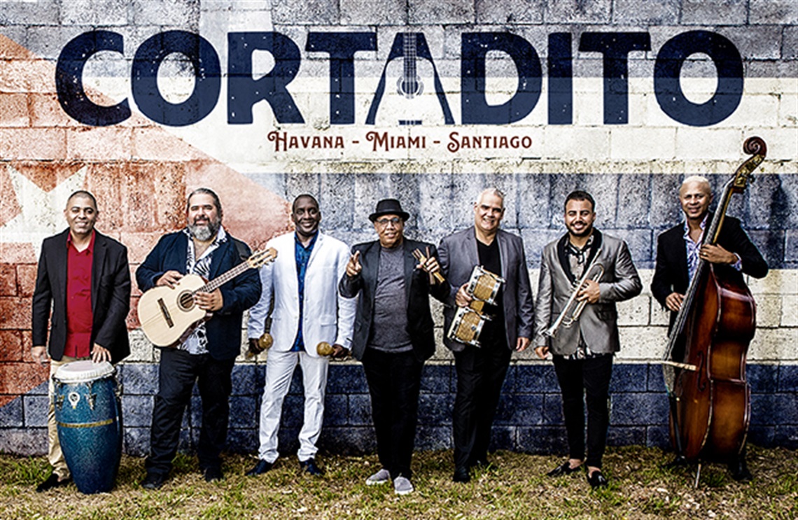 The 7 members of Cortadito holding their instruments. Their band name is featured above them in large letters.