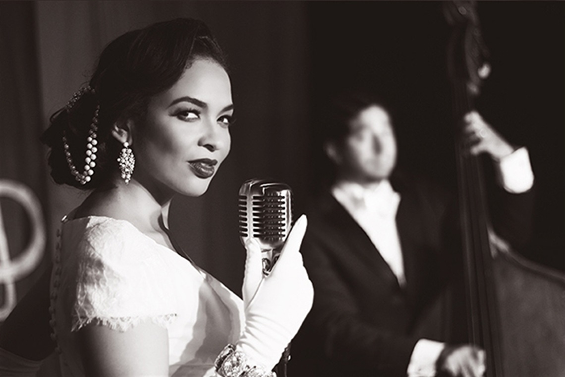 Black and white photo of vocalist Oya in 1940s era costume singing into a retro microphone.