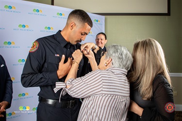 Firefighter Jake Mendez has hit badge pinned on by his grandmother as his mother looks on.