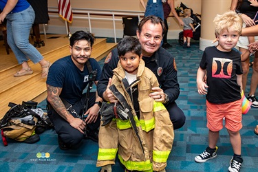 A youngster tries on the heavy fireman's jacket as two firefighters look on.