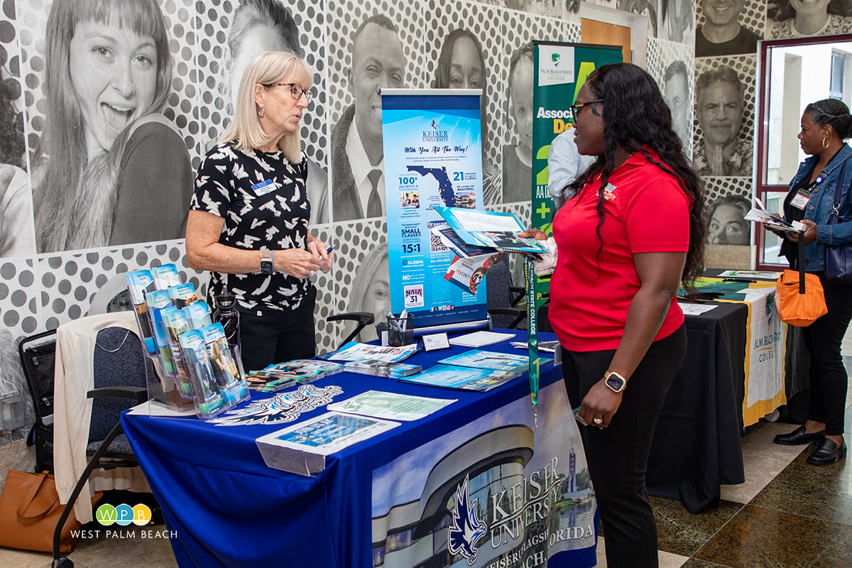 Two ladies standing, Barbara Shafer, left, of Keiser University, speaks with a lady-a