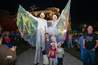Family is dwarfed by two people on stilts with white wings